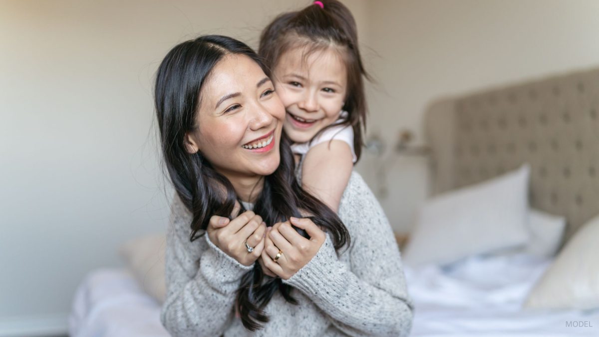 A mother laughing with her little girl on her back smiling. (Models)