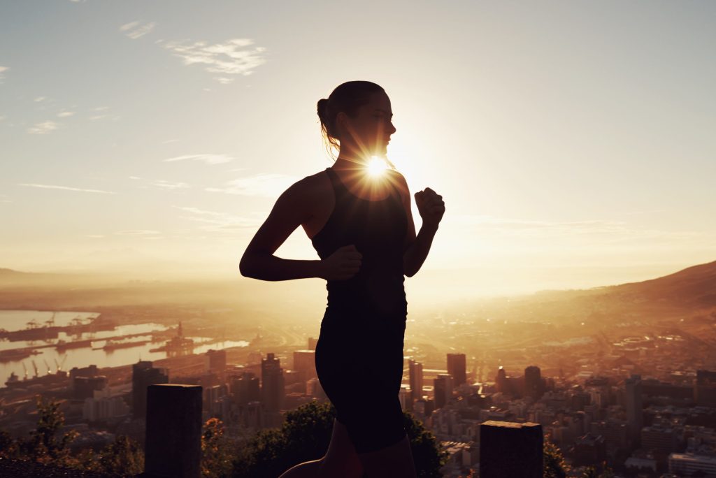 Woman running while sun shines over city skyline