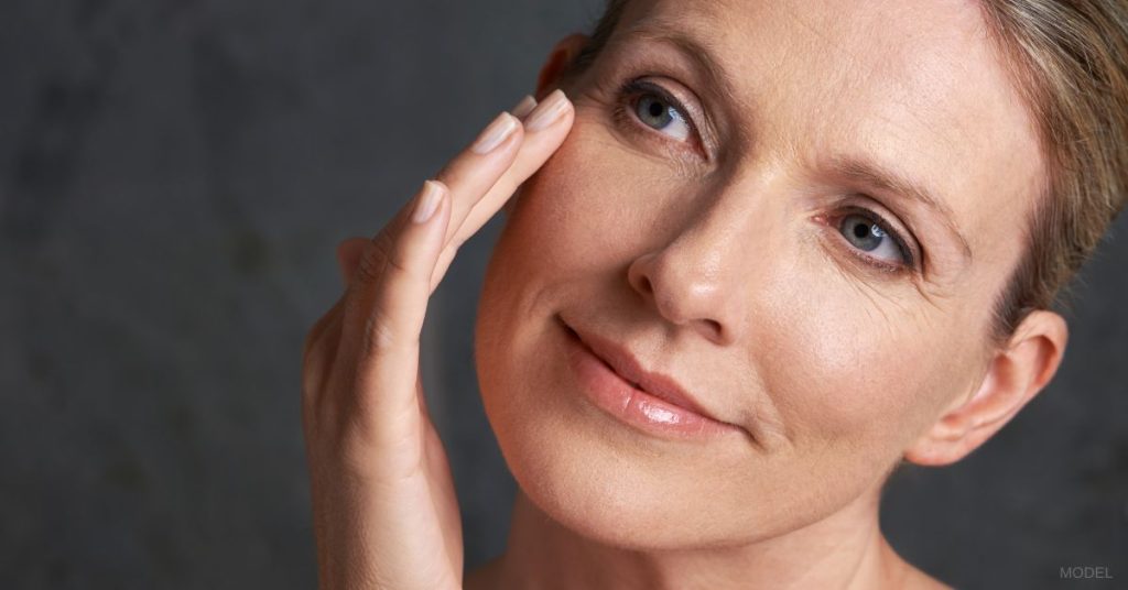 Woman looking off to the side while smiling and touching her face. (MODEL)