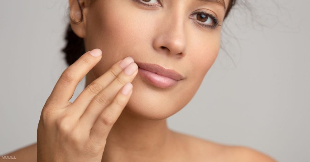 Woman looking at the viewer and touching the side of her lip. (MODEL)