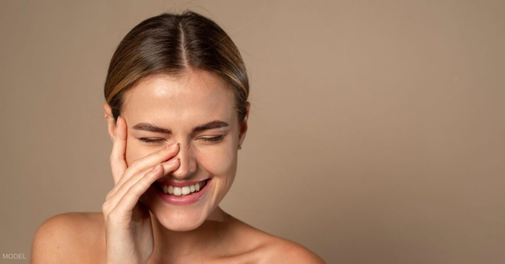 Woman smiling, blushing, looking at viewer and touching her nose. (MODEL)