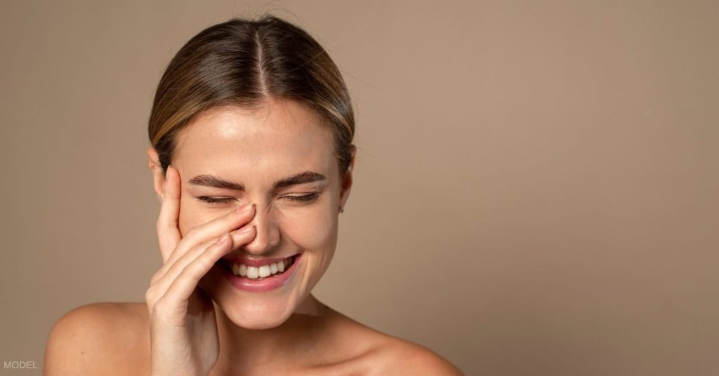 Beautiful woman laughing with her hand by her nose. (MODEL)