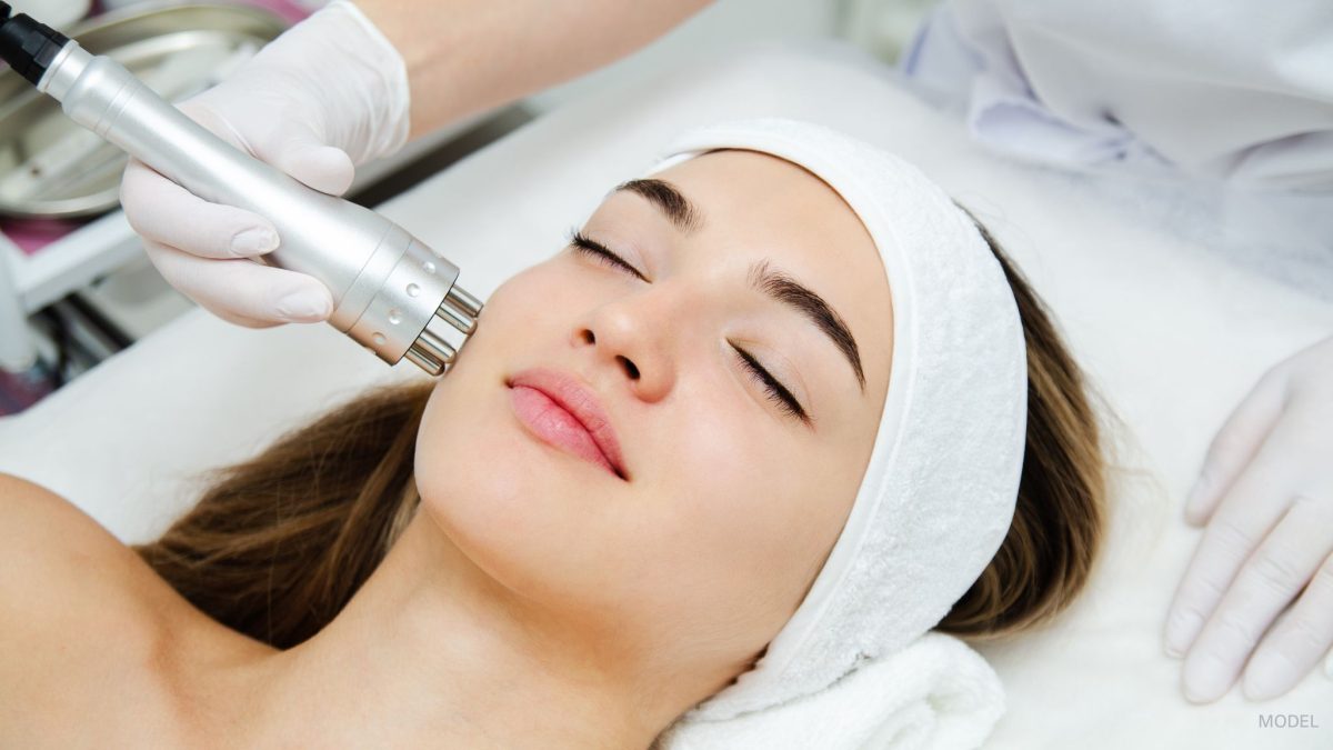 A woman with clear beautiful skin lies back on a pillow while receiving medical spa treatments to her face.